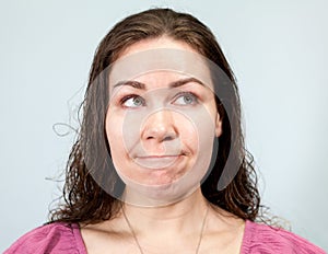 Nervousness and anxiety, pursed lips and a look to the side, portrait of woman on grey background, emotions series