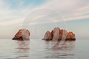 Nes Portes Rocks with a cross on top, north of Paros Island sticking out from perfectly flat Mediterranean Sea, Greece