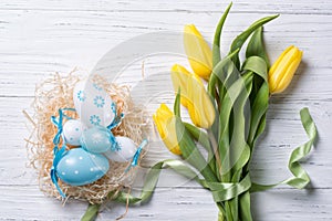 Nest with easter eggs and yellow tulips bouquet on wooden background, top view