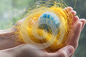 Nest with egg on hands. Decorative blue easter egg in a nest. Blurred background