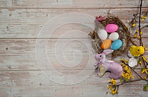 Nest with eggs, chick, pink easter bunny and Forsythia branches with flowers on a wooden background.