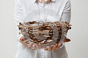 Nest in the hands of a girl in a white shirt on a light background