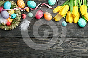 Nest with Ñolorful easter eggs, flowers and feathers on wooden background. Festive tradition. Space for text