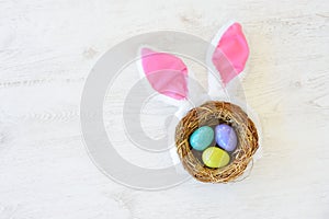 A nest with three colored Easter eggs and bunny ears at home on Easter day. Celebrating Easter at spring.