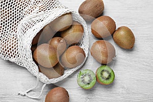 Net bag with cut and whole fresh kiwis on white wooden table, flat lay