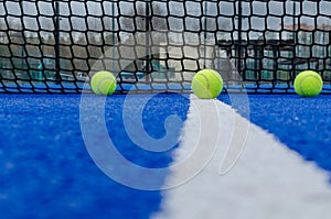 Net of a blue paddle tennis court and five balls near the white line