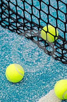 net of a blue paddle tennis court and three balls, racket sports concept