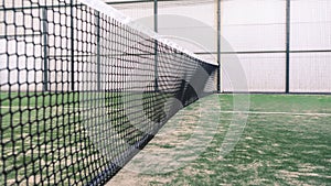 Net and part of green synthetic grass paddle tennis court indoor without people