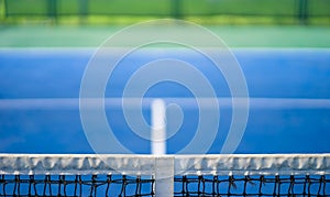 Net of tennis with white stripe in blurred blue and green court, competition concept