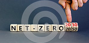 Net-zero 2030 symbol. Concept words Net-zero 2030 or Net-zero 2050 on wooden cubes. Businessman hand. Beautiful grey background.
