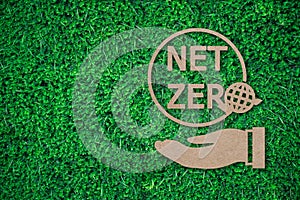 Net zero with earth instead of O over businessman hand paper cut on green grass background with copy space , green energy iconic