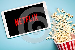 Netflix logo on the screen of a white digital tablet with popcorn