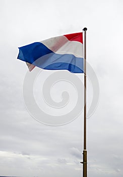 Netherlands. Dutch national flag hoisted on the flagpole that flutters against the background of the cloudy and leaden sky