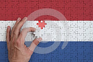 Netherlands flag is depicted on a puzzle, which the man`s hand completes to fold