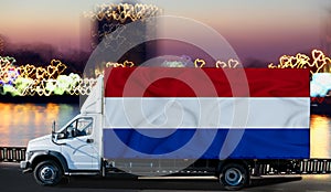 Netherlands flag on the side of a white van against the backdrop of a blurred city and river. Logistics concept