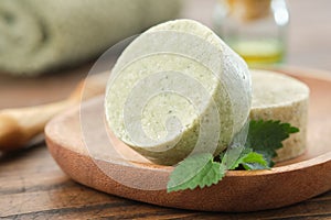 Nettle solid shampoo pieces or homemade natural organic soap bars on wooden soap dish, green nettle leaves.