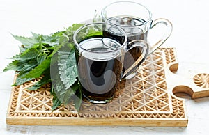 Nettle tea or decoction in glass cups and fresh urtica herb isolated on white wood