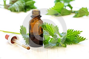 Nettle tincture in a small bottle and fresh leaves on white wood photo