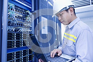 Network administrator holding laptop in hand working Configuration with core switch on rack cabinet in data center