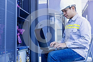 Network administrator holding laptop in hand working Configuration with core switch on rack cabinet in data center