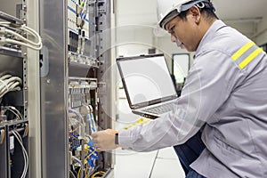 Network administrator holding laptop in hand working Configuration with core switch on rack cabinet in data center