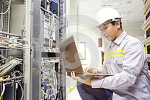 Network administrator holding laptop in hand working Configuration with core switch on rack cabinet in data center