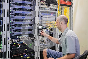 The Network Administrator measures the level of the signal in the optical fiber. The man is working in the server room of the data