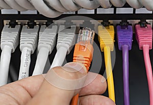 Network engineer connecting an orange ethernet cable into patch panel
