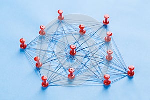 Network with red pins and string, An arrangement of colorful pins linked together with string on a blue background suggesting a