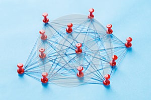 Network with red pins and string, An arrangement of colorful pins linked together with string on a blue background suggesting a