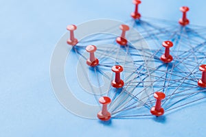 Network with red pins and string, An arrangement of colorful pins linked together with string on a blue background suggesting a