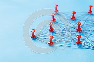 Network with red pins and string, An arrangement of colorful pins linked together with string on a blue background suggesting a