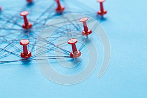 Network with red pins and string, An arrangement of colorful pins linked together with string on a blue background suggesting a