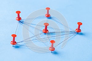 Network with red pins and string, An arrangement of colorful pins linked together with string on a blue background suggesting a