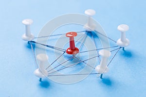 Network with red and white pins and string, An arrangement of colorful pins linked together with string on a blue background