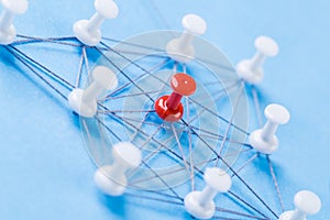 Network with red and white pins and string, An arrangement of colorful pins linked together with string on a blue background