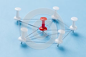 Network with red and white pins and string, An arrangement of colorful pins linked together with string on a blue background