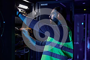 Network technician connecting cables repairing server in data center neon light