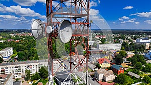 network telecommunication tower with satellite dish on iron construction in living town district below, high view angle photo