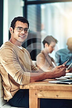 Networking with like-minded people online. a young designer using his cellphone at his desk.