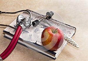 Neurological hammer, medical book and red apple