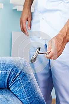 Neurologist checks reflexes hammering knee.