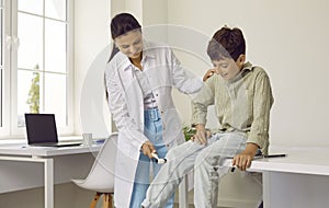 Neurologist examining happy child and using medical hammer to check his knee reflex