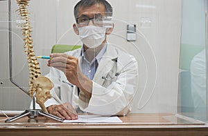 A neurosurgeon pointing at spine vertebra model in medical office photo