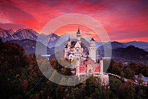 Neuschwanstein fairy tale castle. Beautiful sunset view of the bloody clouds with autumn colours in trees, twilight night, Bavaria