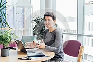 Neutral gender middle aged woman in casual clothing having conversation in office while working laptop on workstation in