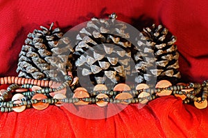 NEUTRAL WOODEN BEADS WITH DRY PINE CONES ON RED DRAPE