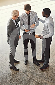 He never fails to impress in the office. High angle shot of a group of businessmen talking together while standing in an