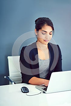 She never gets tired of her job. a happy young businesswoman working behind her laptop in the office.