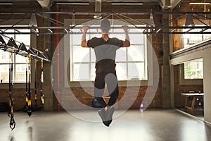 Never give up Back view of strong man doing pull-ups while exercising in the gym